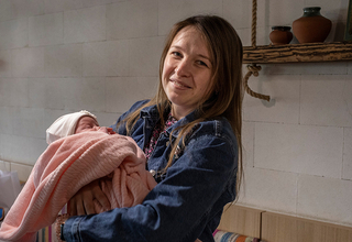 A woman in jeans jacket smiling and holding her newborn in pink cover