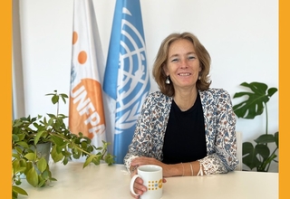 Florence Bauer holding a branded cup with UNFPA logo, and having flags on background