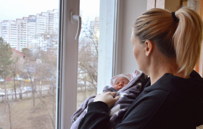 A woman holding her baby, looking outside the window