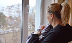 A woman holding her baby, looking outside the window