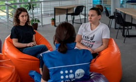 Two young refugee girls speaking with the woman in UNFPA blue jacket
