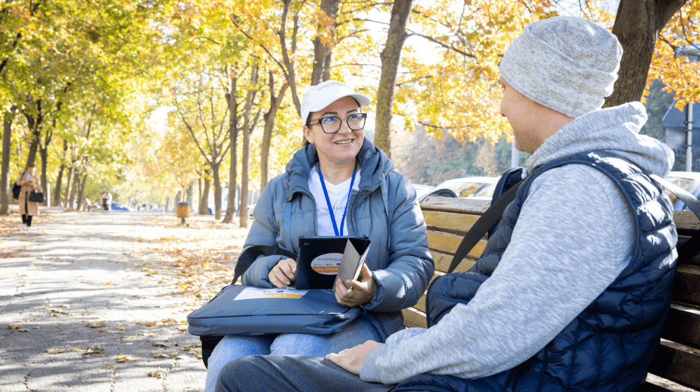 A woman and a man sitting on a bench. The woman is holding a tablet