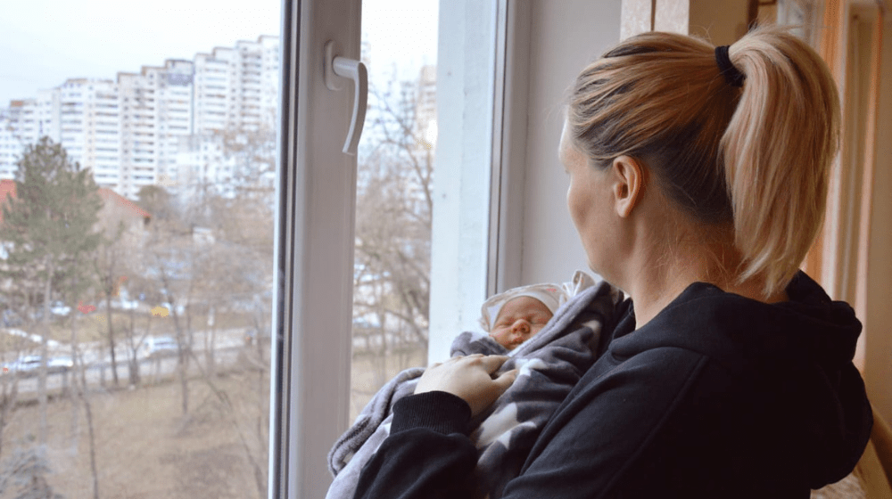 A woman holding her baby, looking outside the window