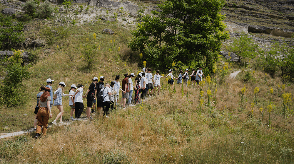 O linie de tineri ucraineni și moldoveni urcând pe poteca de munte cu ochii închiși într-un exercițiu de team-building