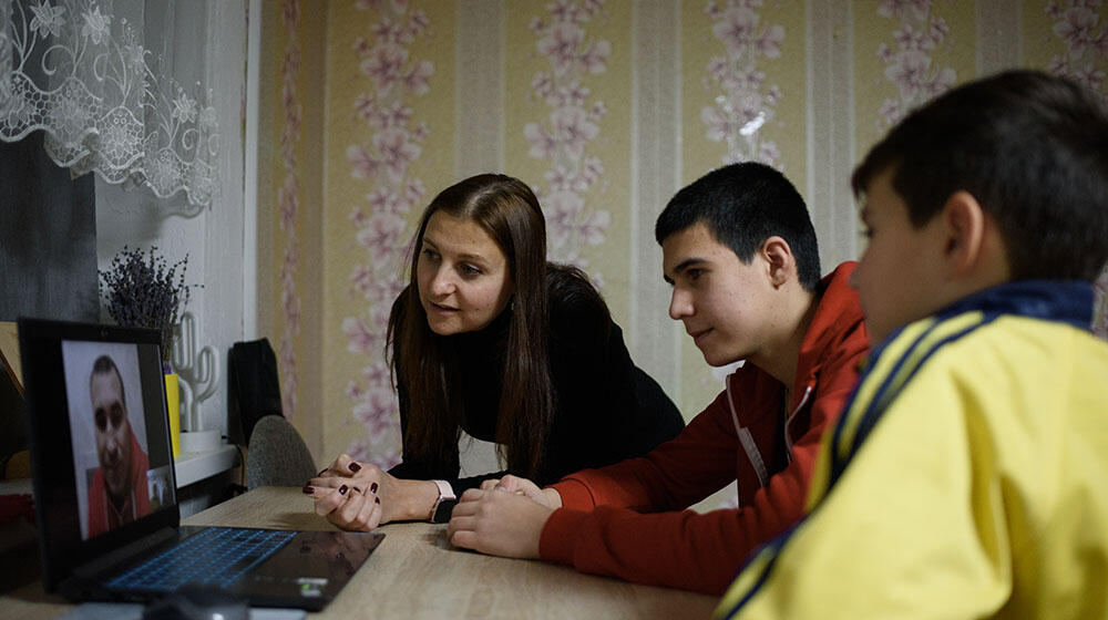 A refugee mother with her two boys speaking to her husband on a computer screen through a video call