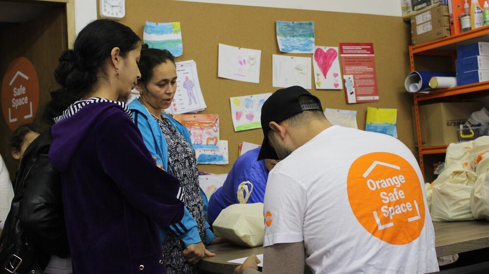 A Roma man writing information on paper with two Roma women standing near him.