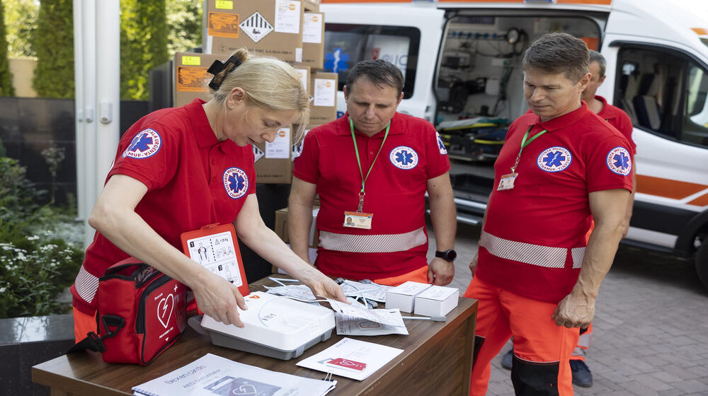 Trei lucrători de la ambulanță, o femeie și doi bărbați, inspectează defibrilatoarele.